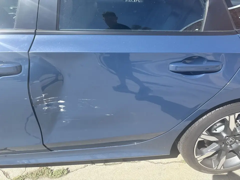 Before: close-up of creased left rear door and rear wheel on a 2025 Honda Civic