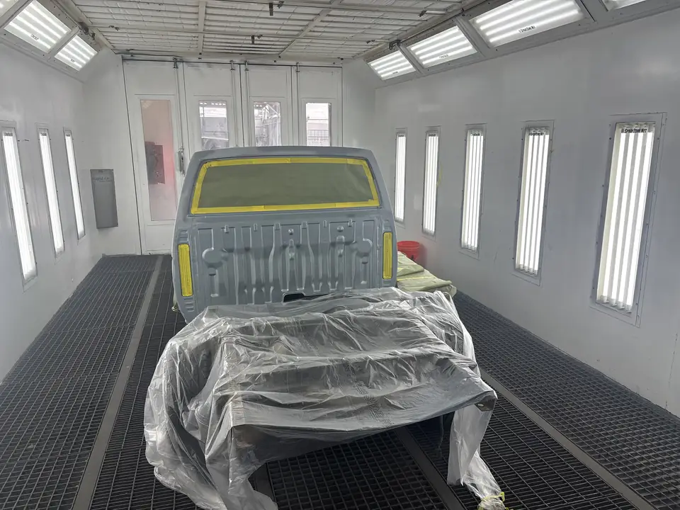 Rear view of a primed pickup truck, masked with tape and plastic sheeting, inside the downdraft paint booth at Clairemont Collision in San Diego