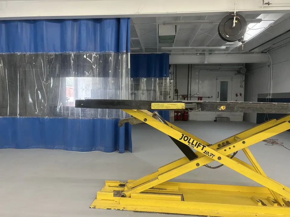 Yellow Jollift scissor lift in the Clairemont Collision prep area in Kearny Mesa, beside blue and clear curtained paint prep stations